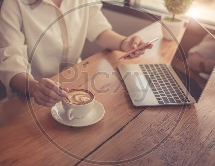 Close Up Of Business Woman Working With Laptop And Drinking Coffee In Office. Business And Lifestyles Concept. Entrepreneur And Freelance Theme. Selective Focus On Coffee Cup