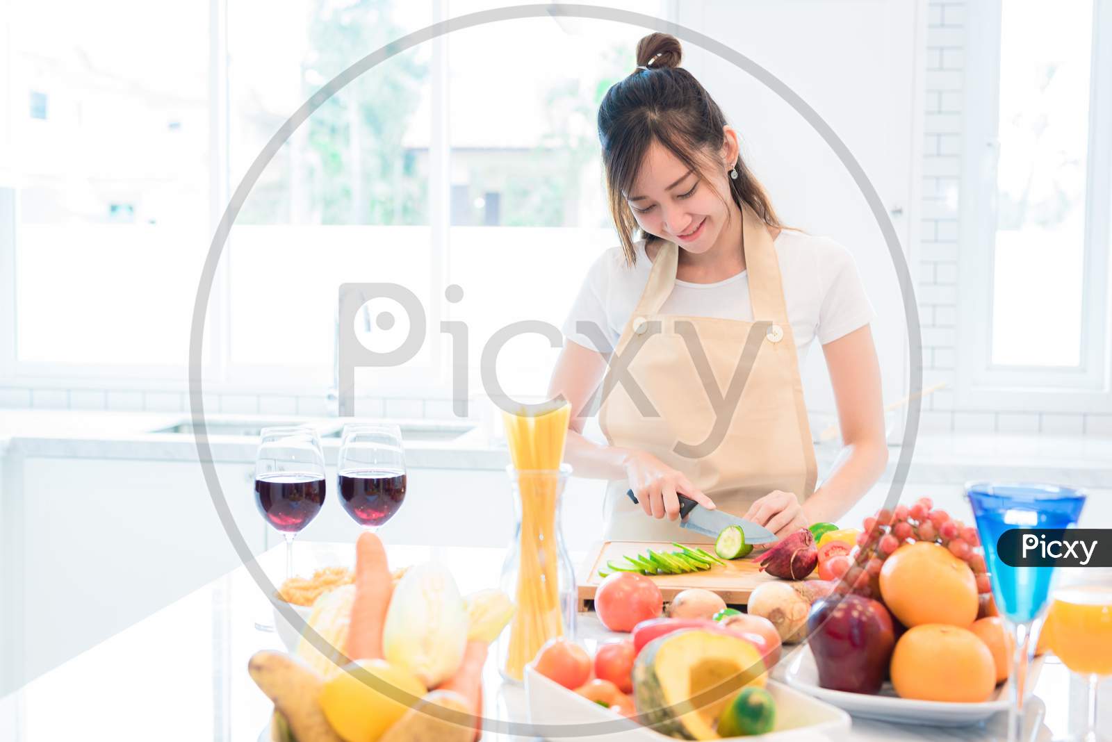 Woman Cooking And Slicing Vegetable In Kitchen Room With Full Of Food And Fruit On Table. Holiday And Happiness Concept.