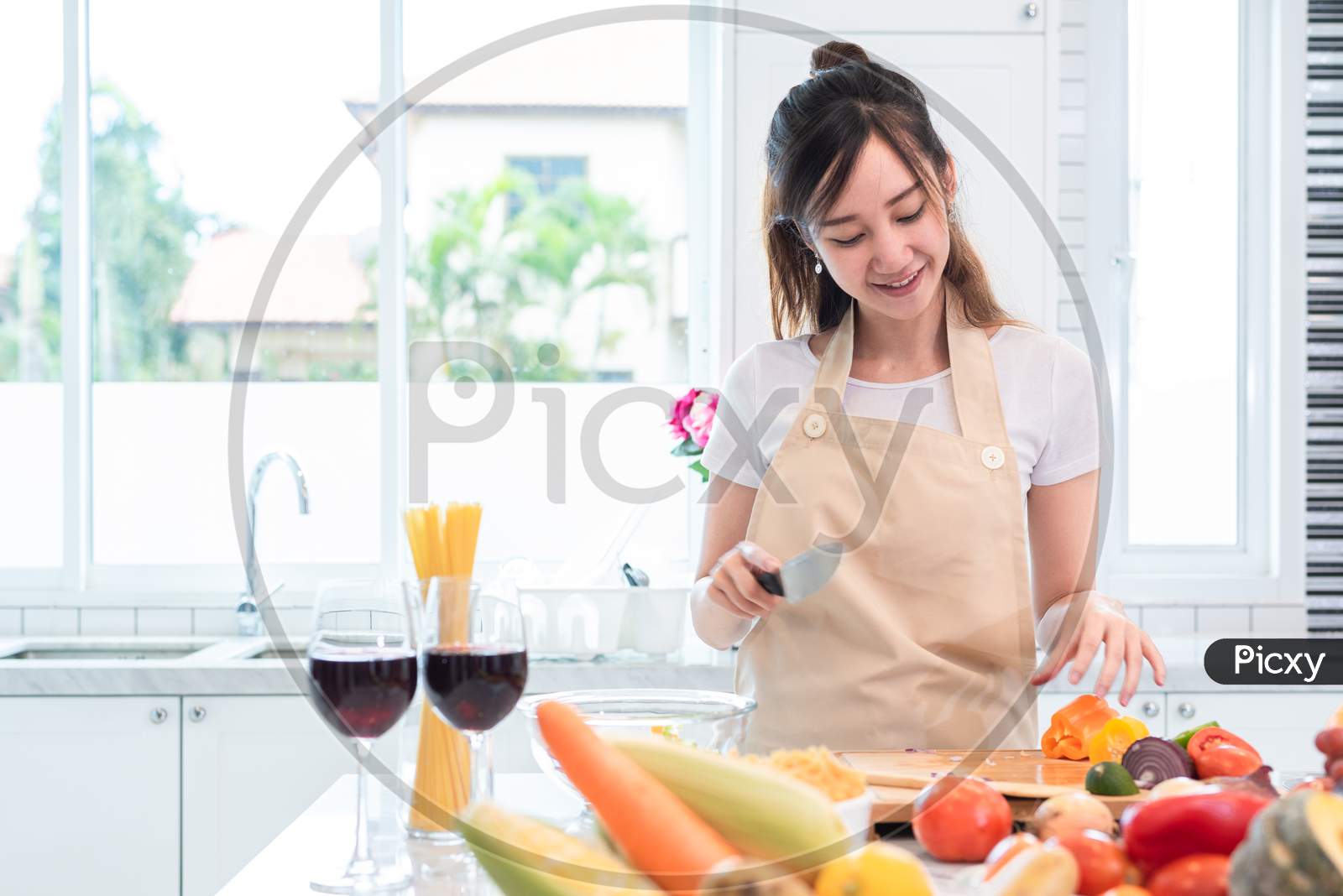 Asian Beauty Woman Cooking And Slicing Vegetable In Kitchen Room With Full Of Food And Fruit On Table. Holiday And Happiness Concept. People And Lifestyles Concept. Family And Dinner Party Theme.