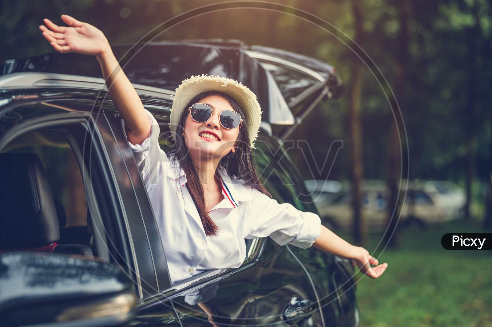 Happy Woman Waving Hand Outside Open Window Car With Meadow And Mountain Forest Background. People Lifestyle Relaxing As Traveler On Road Trip In Holiday Vacation. Transportation And Weekend Travel