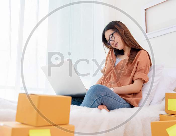 Beauty Asian Woman Using Laptop And Calling Phone On Bed. Business And Technology Concept. Delivery And Online Shopping Concept. Post And Service Theme. People Lifestyle Remote Work From Home