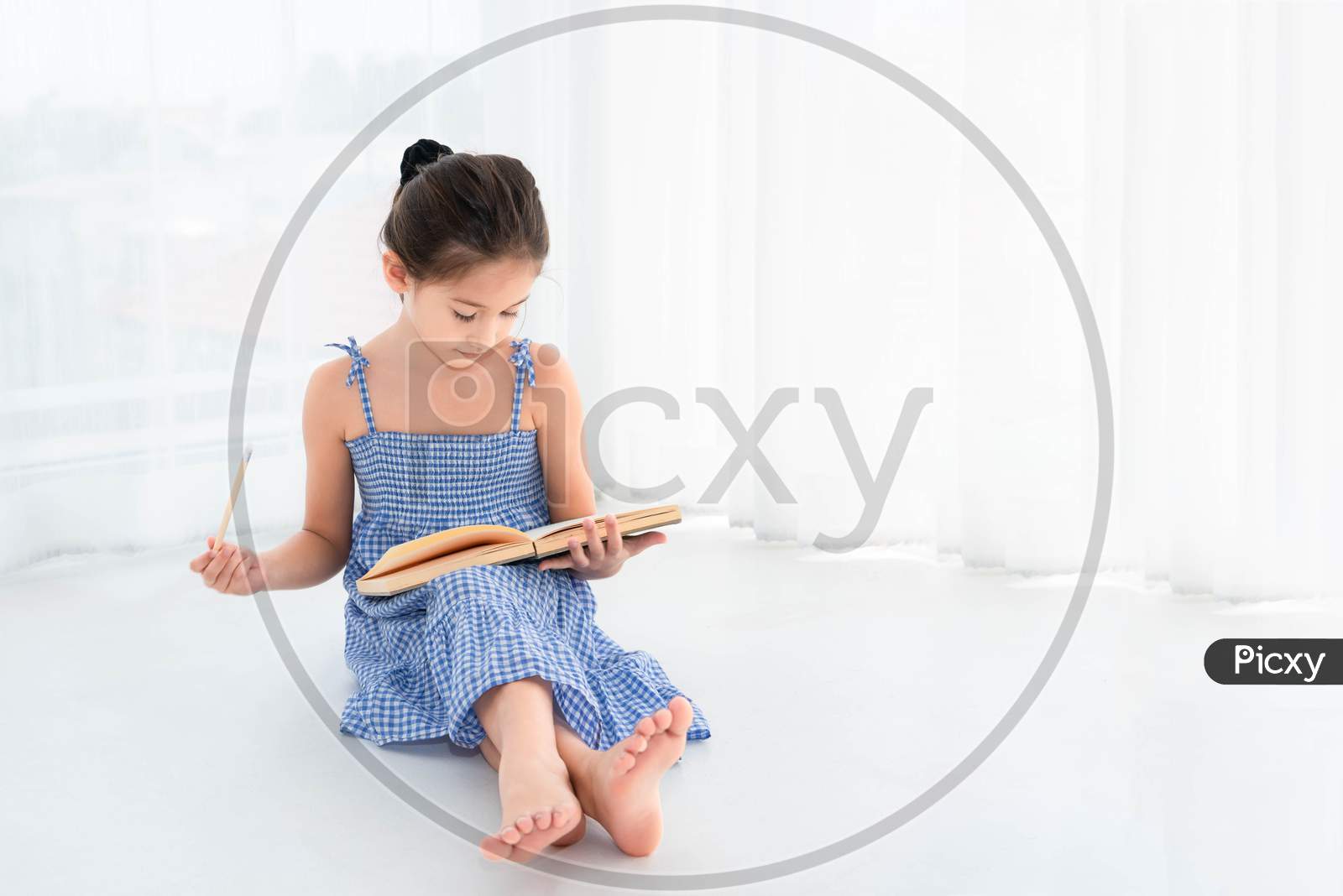Cute Girl Reviewing Homework And Lessons With Notebook And Wooden Pencil In Hand In White Bedroom Background At Home. Education And People Lifestyles. Self-Learning Concept. Back To School Theme.