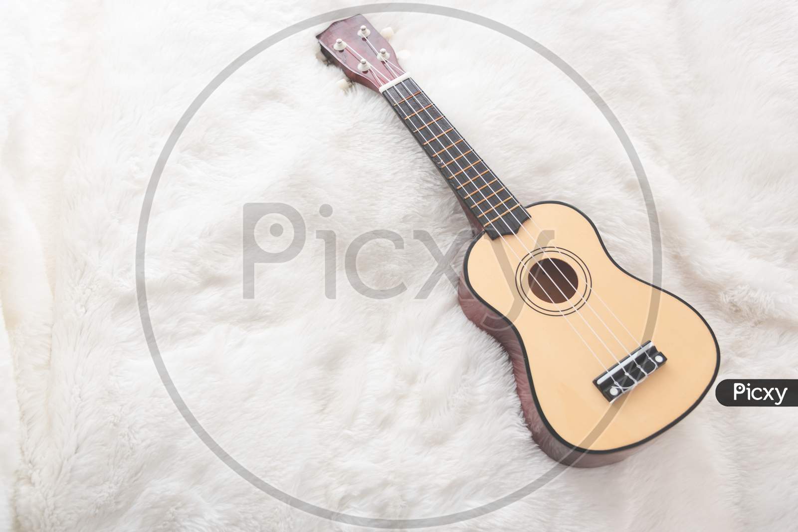 Small Guitar On White Wool. Musical Instrument And Leisure Concept. Travel And Relax Theme.