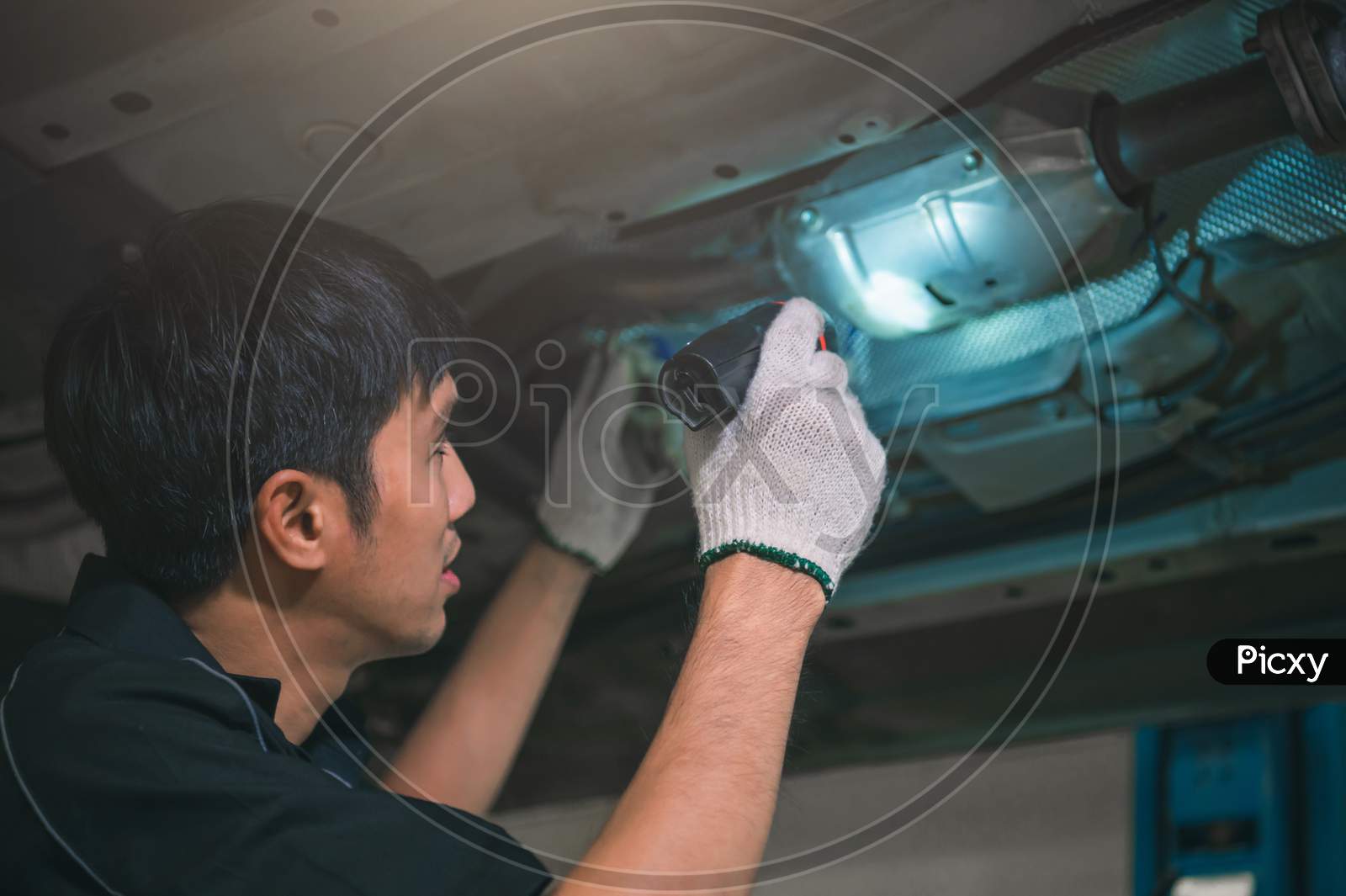 Asian Male Mechanical Hold And Shining Flashlight To Examine Car Under Chassis Of Automotive Vehicle. Safety Suspension Inspection Check Service Maintenance For Customer Before Road Trip Concept
