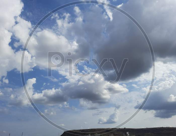 White and dark clouds, blue sky behind with a small mountain and buildings with fresh and clean air atmosphere