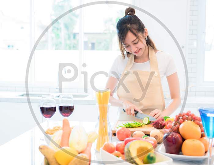 Woman Cooking And Slicing Vegetable In Kitchen Room With Full Of Food And Fruit On Table. Holiday And Happiness Concept.