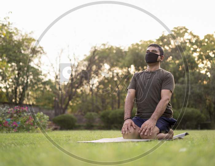 Mid-Aged Man Doing Yoga In A Park Covered With Trees On International Yoga Day.