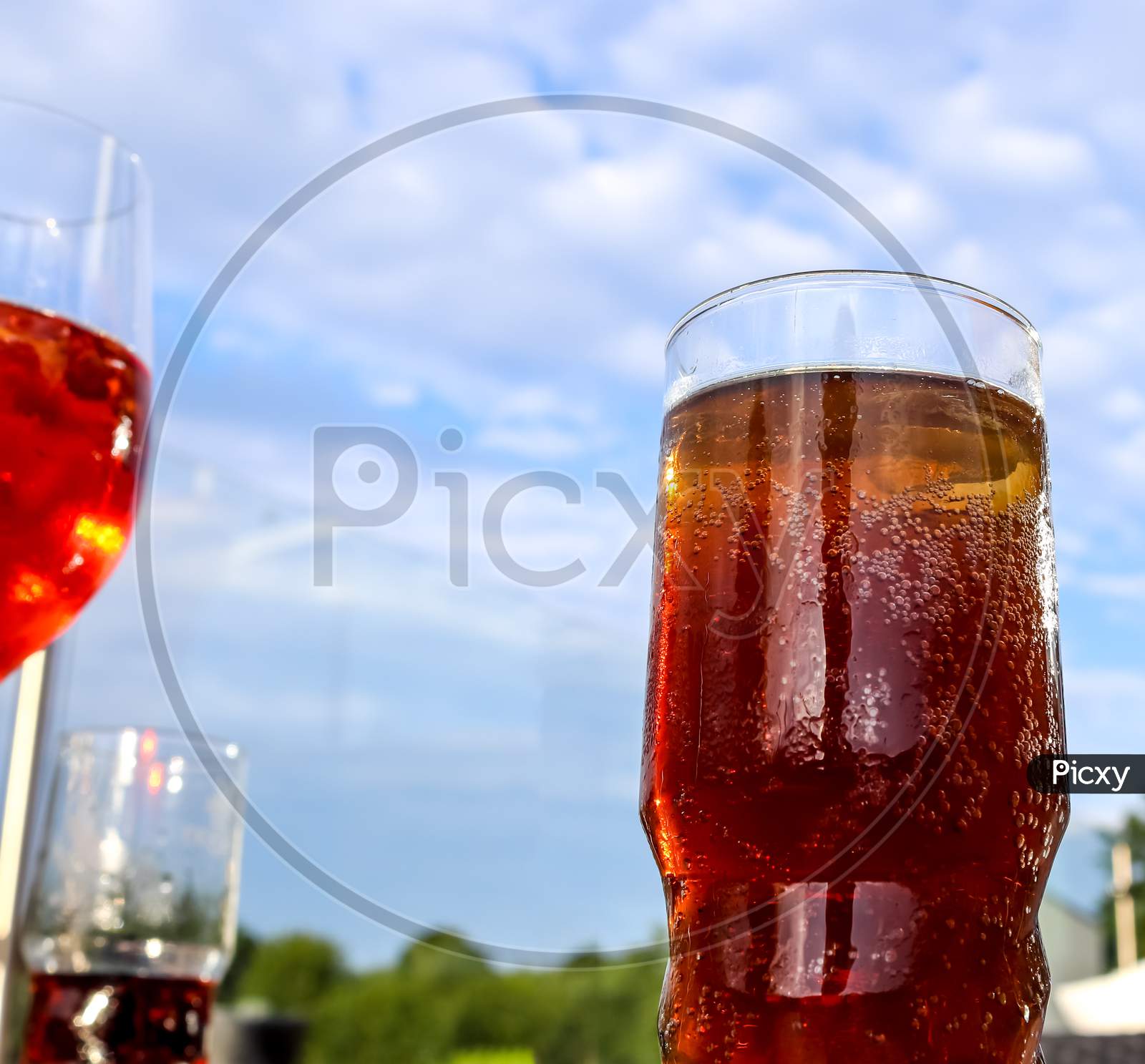 Refreshing orange summer cocktails with cola and ice against a blue sky background. Close up view.
