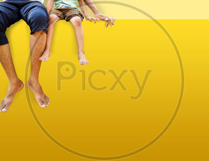 Father And Daughter Sitting On Yellow Color Wall And Hanging Feet Outdoor