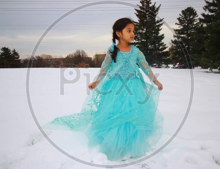 A little girl in a beautiful blue frock playing in the snow