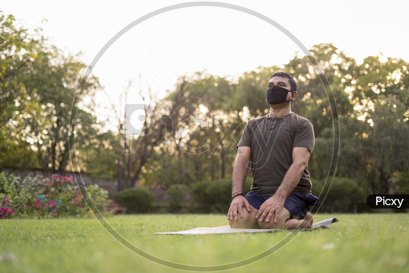 Mid-Aged Man Doing Yoga In A Park Covered With Trees On International Yoga Day.