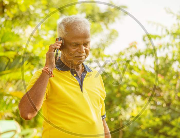 Elder Man Busy In Mobile - Healthy Senior Indian On Phone Outdoor At Park, Morning - Happy Male Parent Talking On Phone.