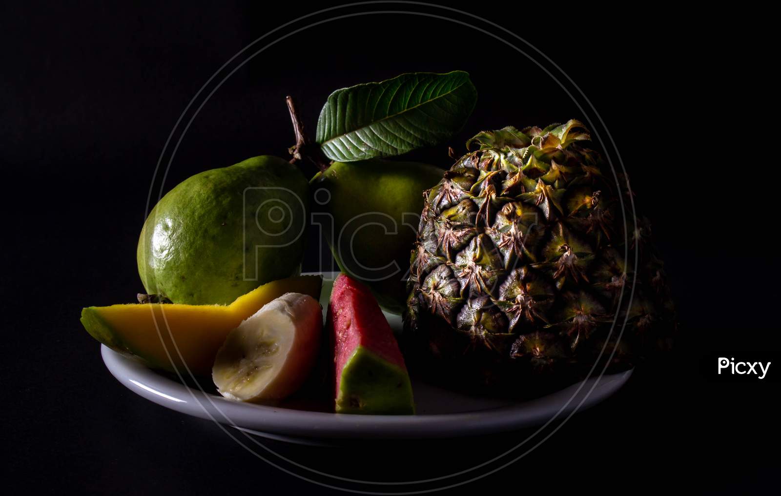 Whole And Cut Varied Fruits On A Plate. Neutral Black Background With Pictorial Lighting. Vegetarian Or Vegan Breakfast Concept.