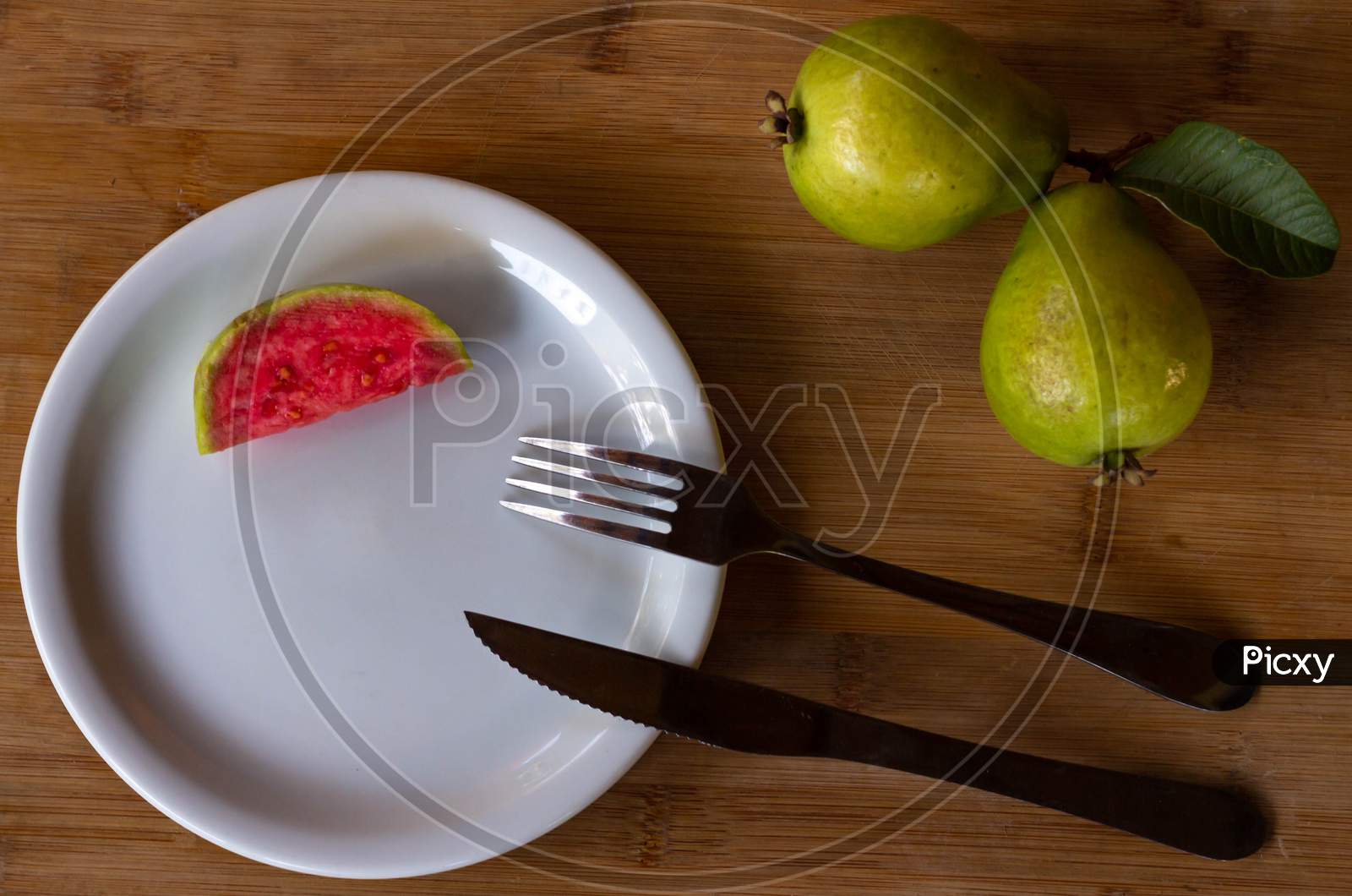 Two Exotic Fruits From Brazil Called Guava. A Piece Of Cut Fruit On A Plate With Fork And Knife. Wood Background.