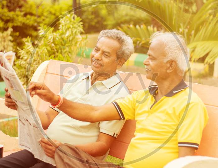 Two Happy Senior Men Reading Newspaper At Park Outdoor - Elderly Friends Enjoying Moring News - Concept Of Happy Older Men Lifestyle.