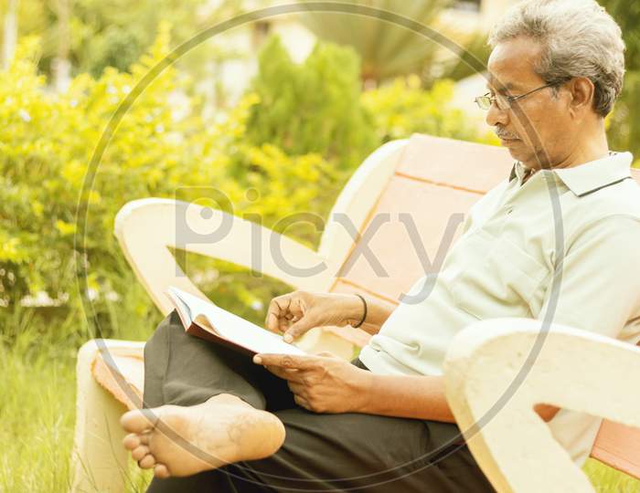 Healthy Looking Senior Man In Late 70S Sitting In Garden At Home And Reading Book, Outdoor - Old Man Relaxing At Park By Seriously Reading Book.