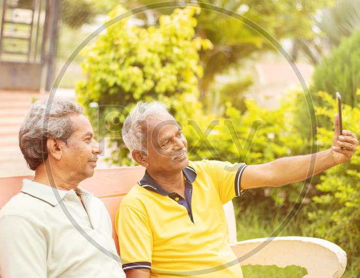 Two Senior Happy Friends Taking A Selfie At Park, Outdoor - Elderly Men Making Video Call - Concept Of Active And Fun Elderly People Using New Technologies
