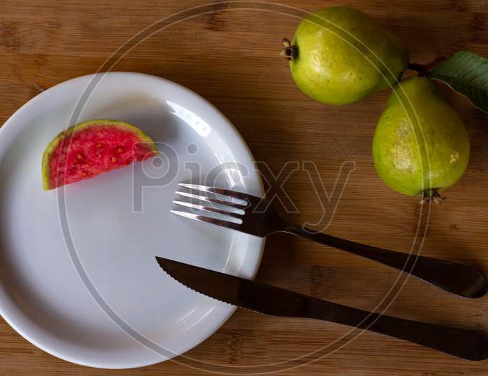 Two Exotic Fruits From Brazil Called Guava. A Piece Of Cut Fruit On A Plate With Fork And Knife. Wood Background.