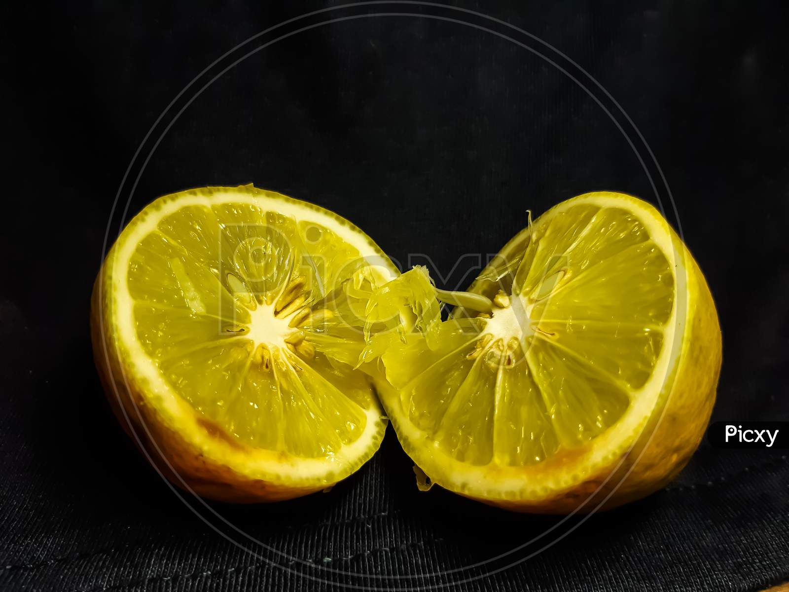 A Lemon Is Cut In The Middle And It Is On A Black Background.