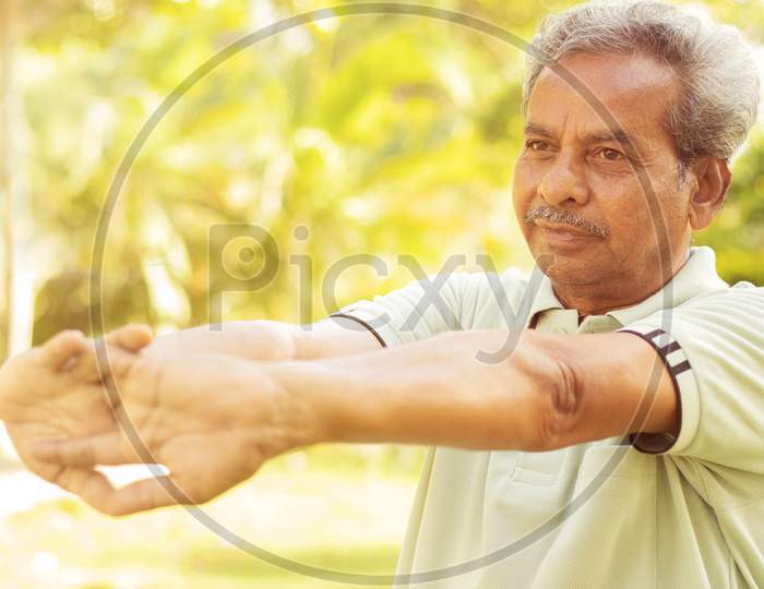 Senior Man Stretches Hands Before Exercise - Concept Of Elderly Person Fitness Outdoor - 60S Person Doing Yoga Asana At Park.