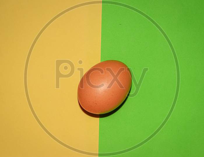 Brown colour egg on yellow green two colour background . Top view.