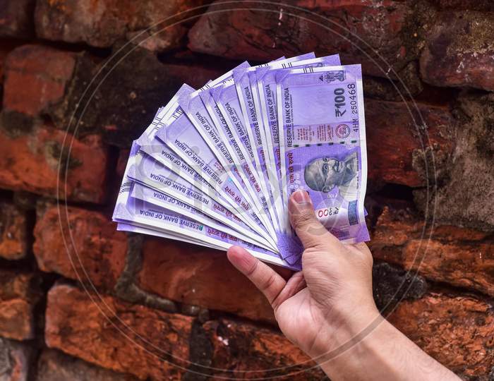 Hand with hundred Indian rupee notes on brick background