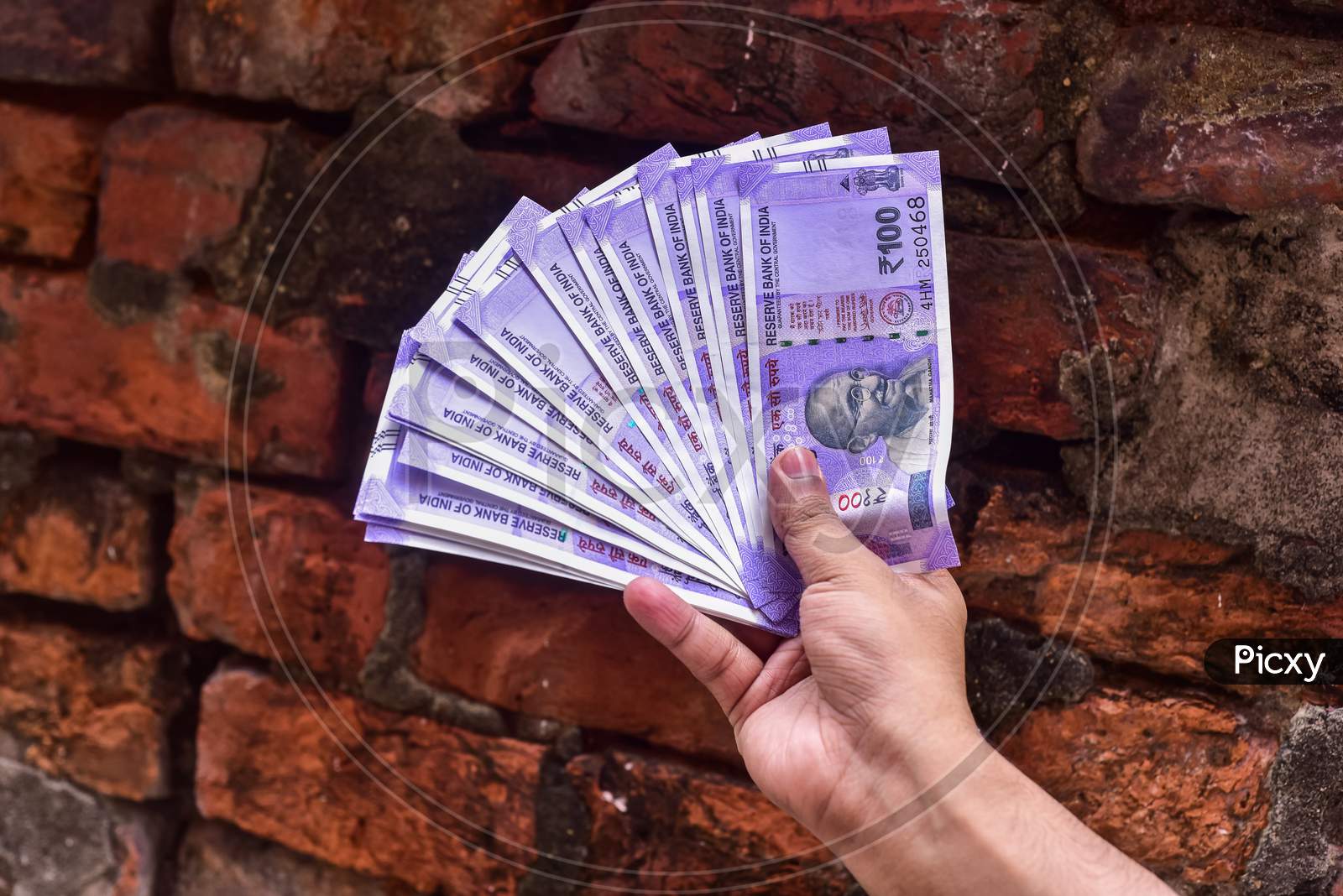 Hand with hundred Indian rupee notes on brick background