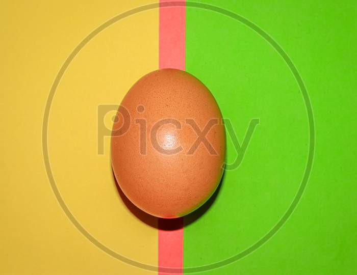Brown colour egg on yellow red and green colour background . Top view.