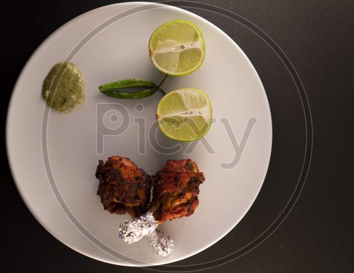 Chicken legs with green spicy sauce, green chilli and lime on a white plate on a black background.