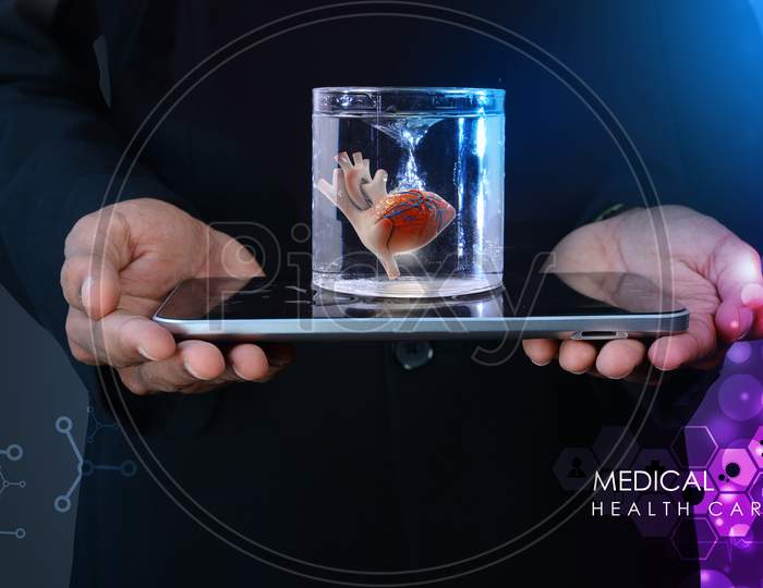 Man Is Holding A Heart In Glass Of Water  And Tablet Computer