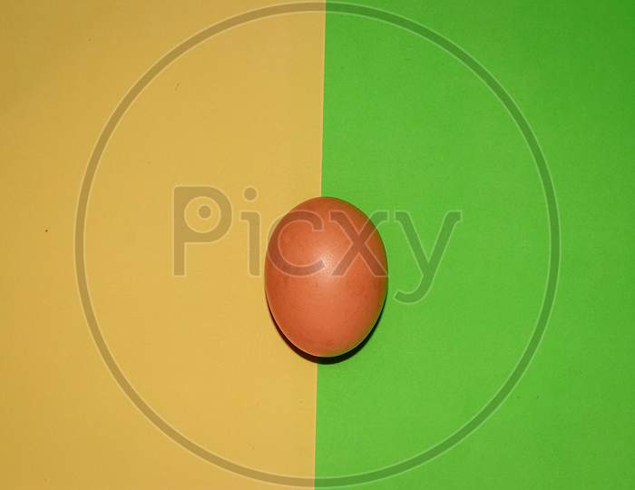 Brown colour egg on yellow  green two colour background . Top view.