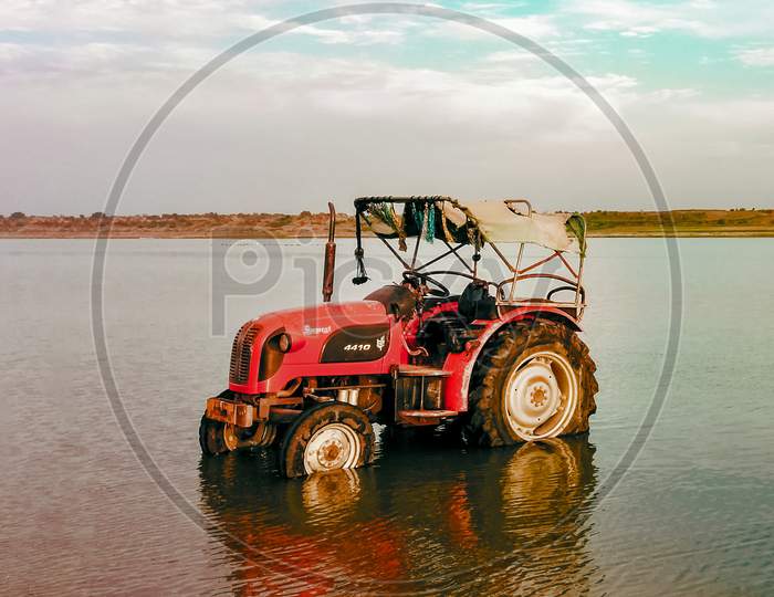 Cleaned Tractor Standing In Water, Reflection Seen In River Water.