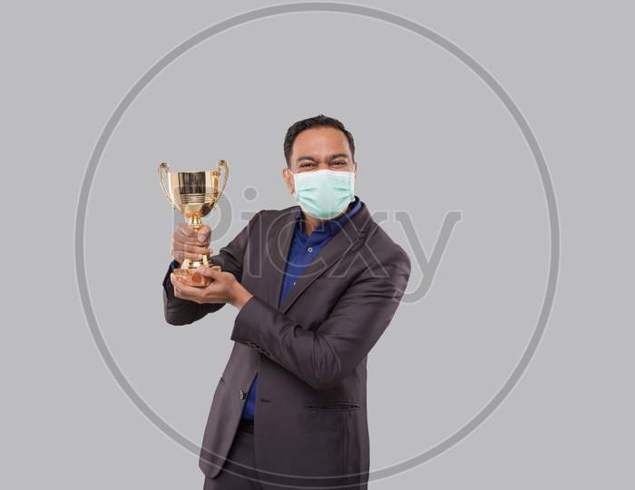 Businessman Holding Trophy Wearing Medical Mask. Indian Business Man Standing With Trophy In Hands