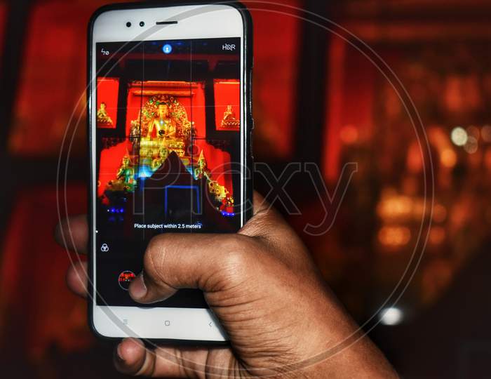 A Photo Of Buddha Statue Taken In Mobile Is Captured . The Golden Statue Of Buddha In Focus