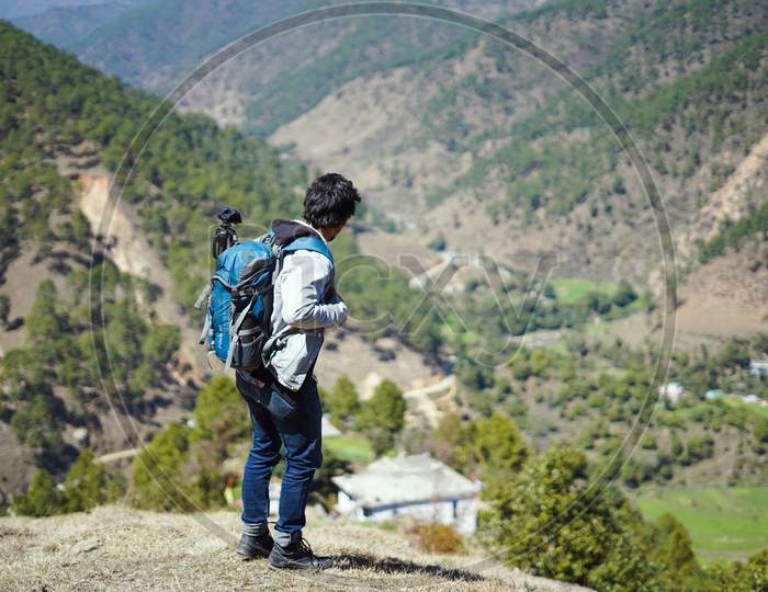 Young Handsome Indian Boy Standing On The Top Of The Mountain With A Bag Pack , Traveling And Wanderlust.