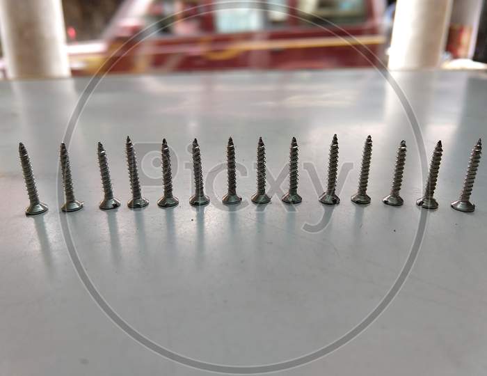 Fourteen Numbers Of Small Size Screws Places Upside Down In A Row On A White Table