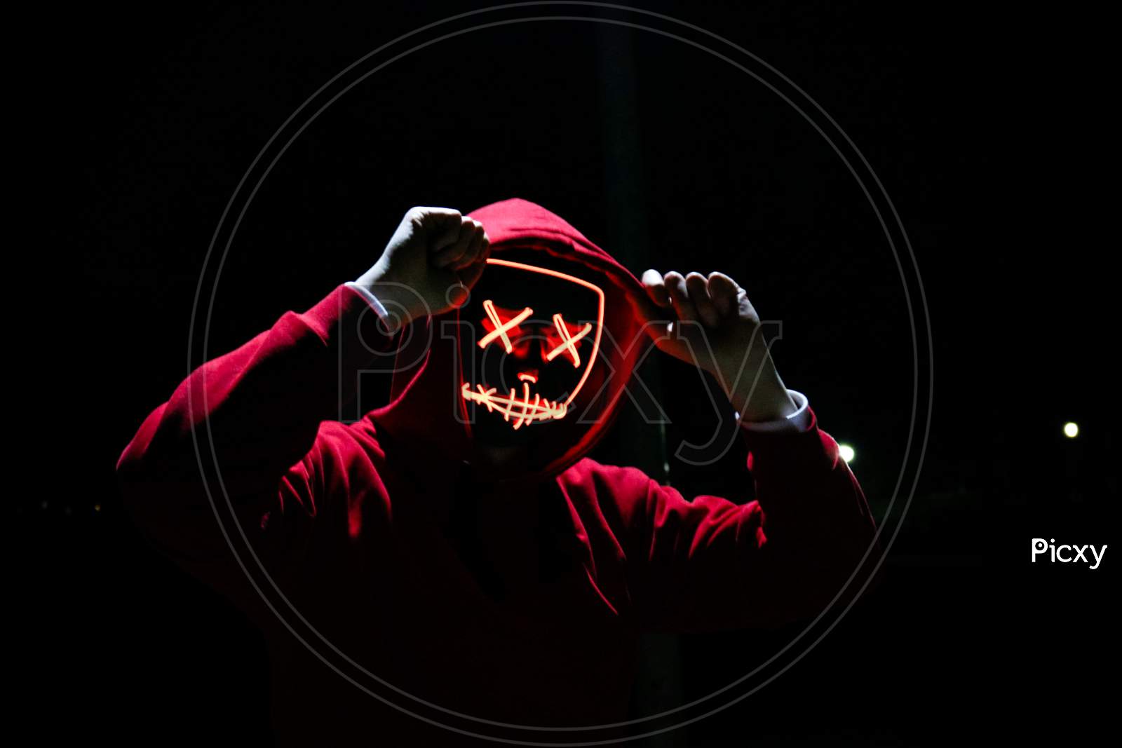 A Man Wearing A Red Hoodie With Red Glowing Mask In The Dark Background. Halloween And Horror Concept.