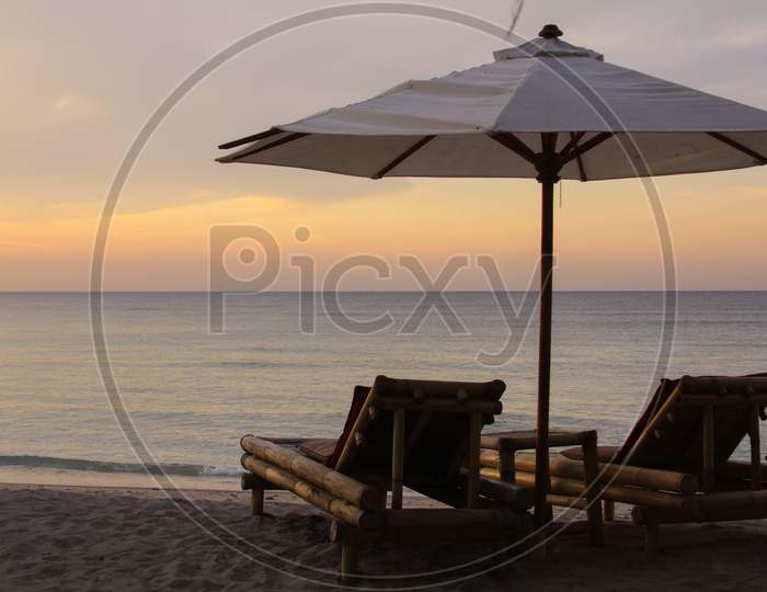 Tropical Umbrella And Bamboo Long Chairs On Beach