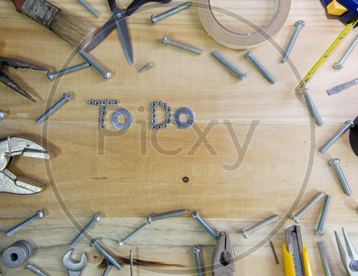 A High Angle Shot Of The Phrase "To Do" Made Of Screws Surrounded By Instruments On A Wooden Surface For Planning The Work