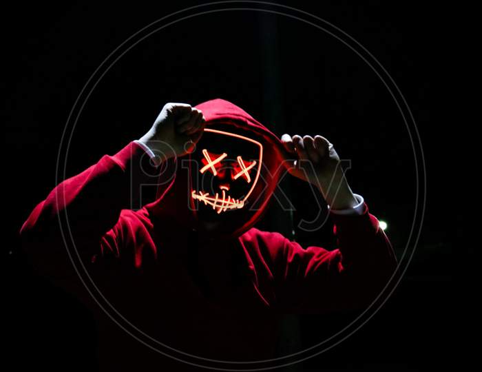 A Man Wearing A Red Hoodie With Red Glowing Mask In The Dark Background. Halloween And Horror Concept.