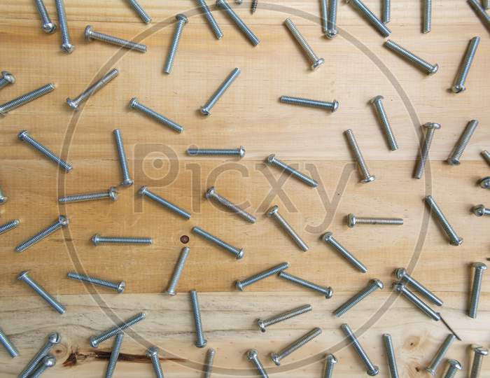 Numerous Silver Screws Scattered On A Light Wooden Bench. Pine Wood.