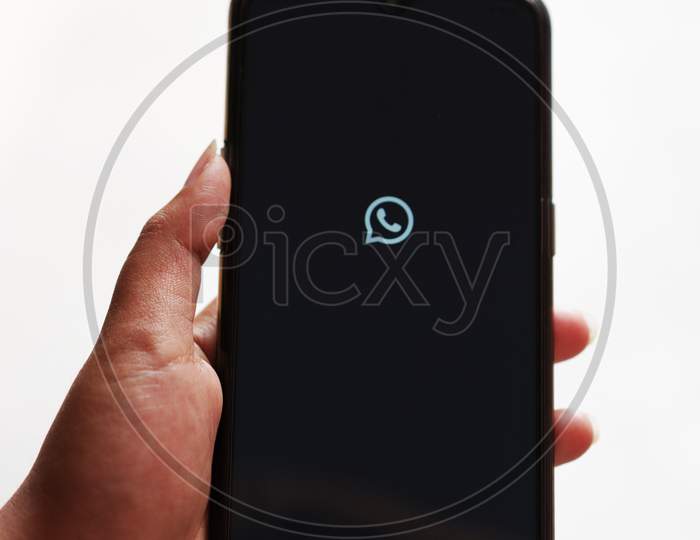 Whatsapp logo/icon on screen of a smart phone, held in hand against white background with copy space