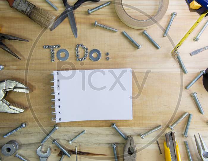 A High Angle Shot Of The Phrase "To Do" Made Of Nuts And Washers And A Blank Notebook On A Wooden Surface For Planning The Work