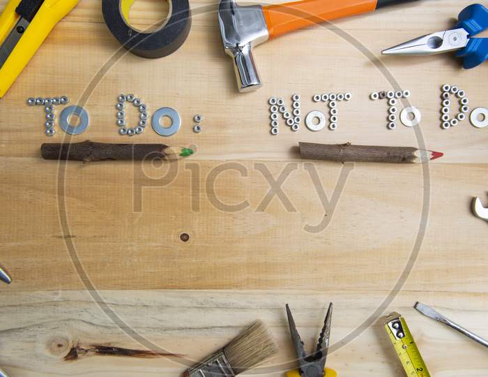 Top View Of The Phrases "To Do" And "Not To Do" Made Of Nuts And Washers On A Wooden Surface Underlined By Rustic Wooden Pencils. Construction Tools Framing Wooden Background Shot From Above.