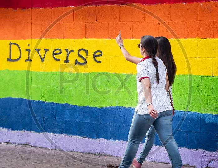 Wall With The Colors Of The Lgbt Flag And Two Women Walking Together