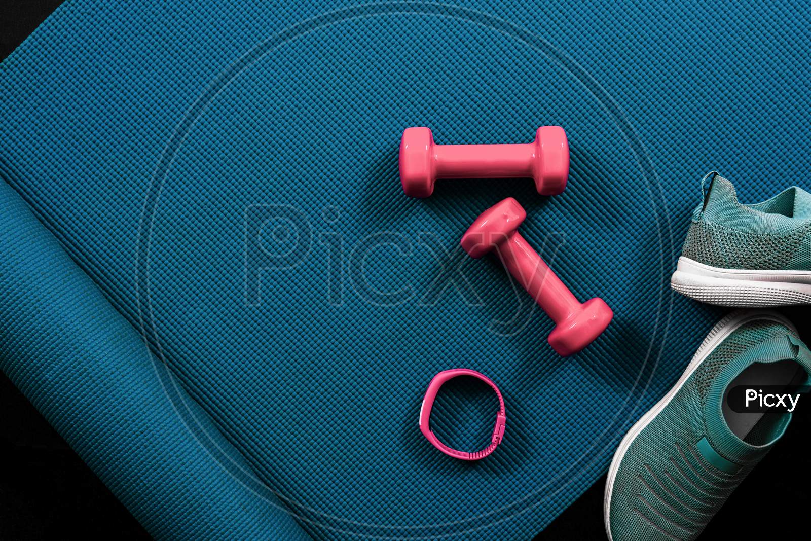 Fitness flat lay with dumbbells, shoes, activity tracker and yoga mat. Textured blue background with copy space