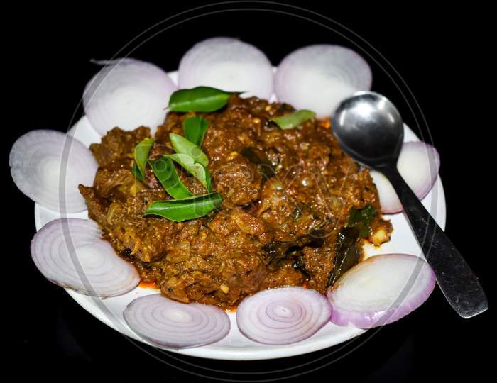 South Indian Cuisine Kerala Style Beef Fry / Roast. Traditional Style Meat Roast. Garnished With Onion Slices And Curry Leaves. Black Background. Selective Focus Photograph.