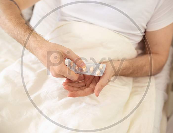 Man Taking Pills In Bed. Sick Man At Home Staying In Bed. Self Treatment Tablets Close Up