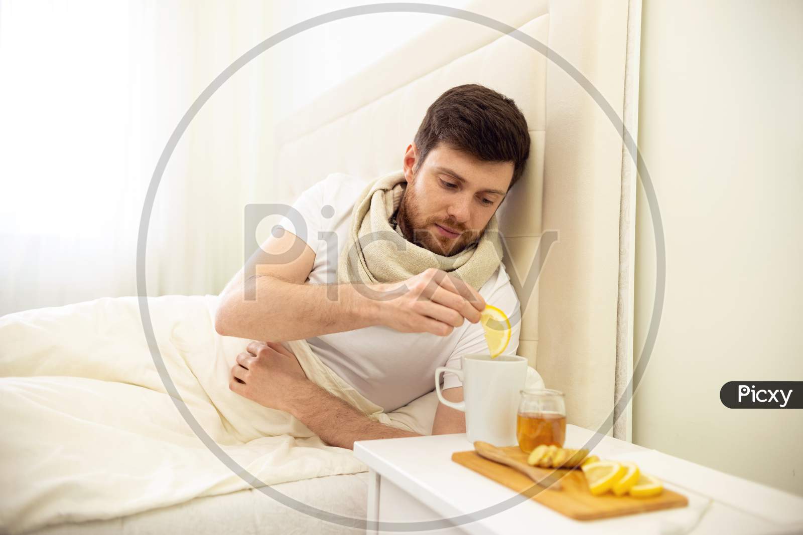Sick Man In Bed Adding Lemon Into Tee. Man Ill In Bed Self Healing. Self Treatment At Home. Man Drinking Hot Tea In Bed.