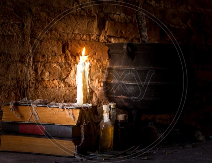 Spell Of Witch Night With Candles And Pot With Fire Between Cobwebs And Ancient Earth